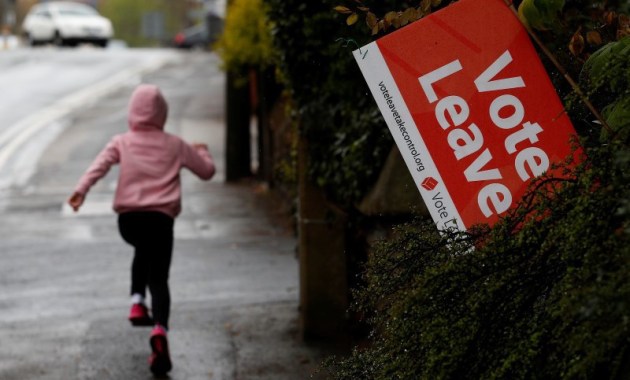 A girl runs past a Vote Leave sign, protruding from the garden of a house in Altrincham